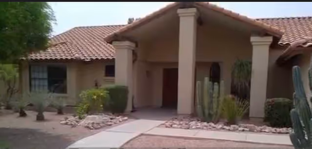 Front entrance of a beige stucco senior living building with pillars and desert landscaping