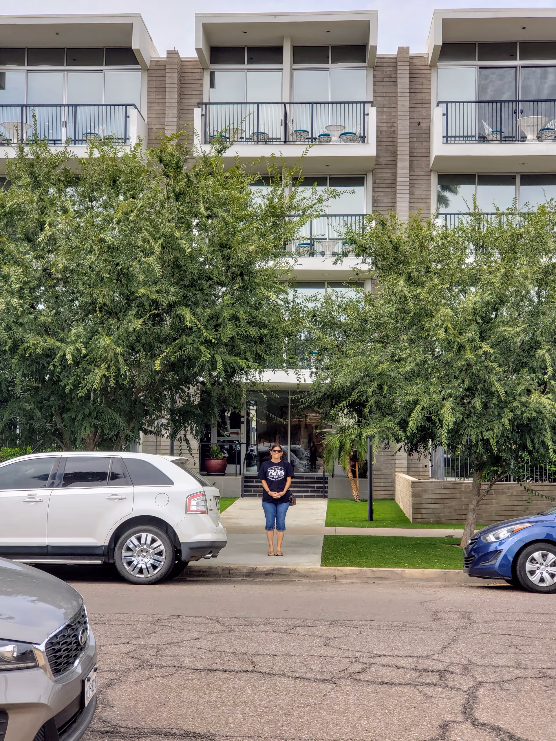 Three-story senior living building with balconies, trees, and a person near the entrance.