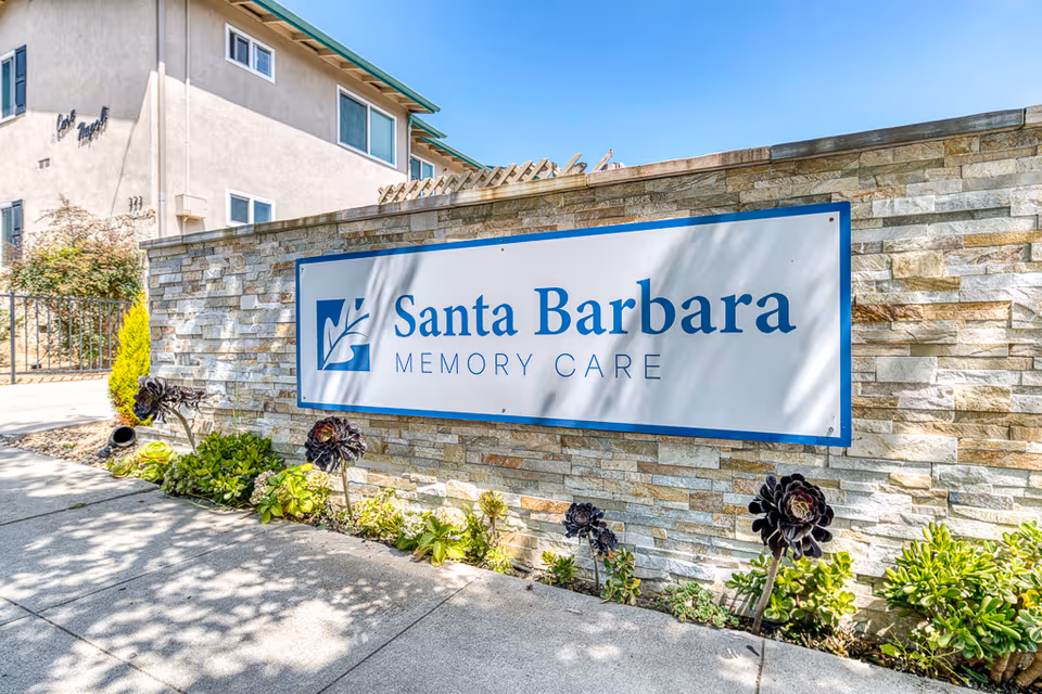 Exterior view of Santa Barbara Memory Care sign on a stone wall with the building behind