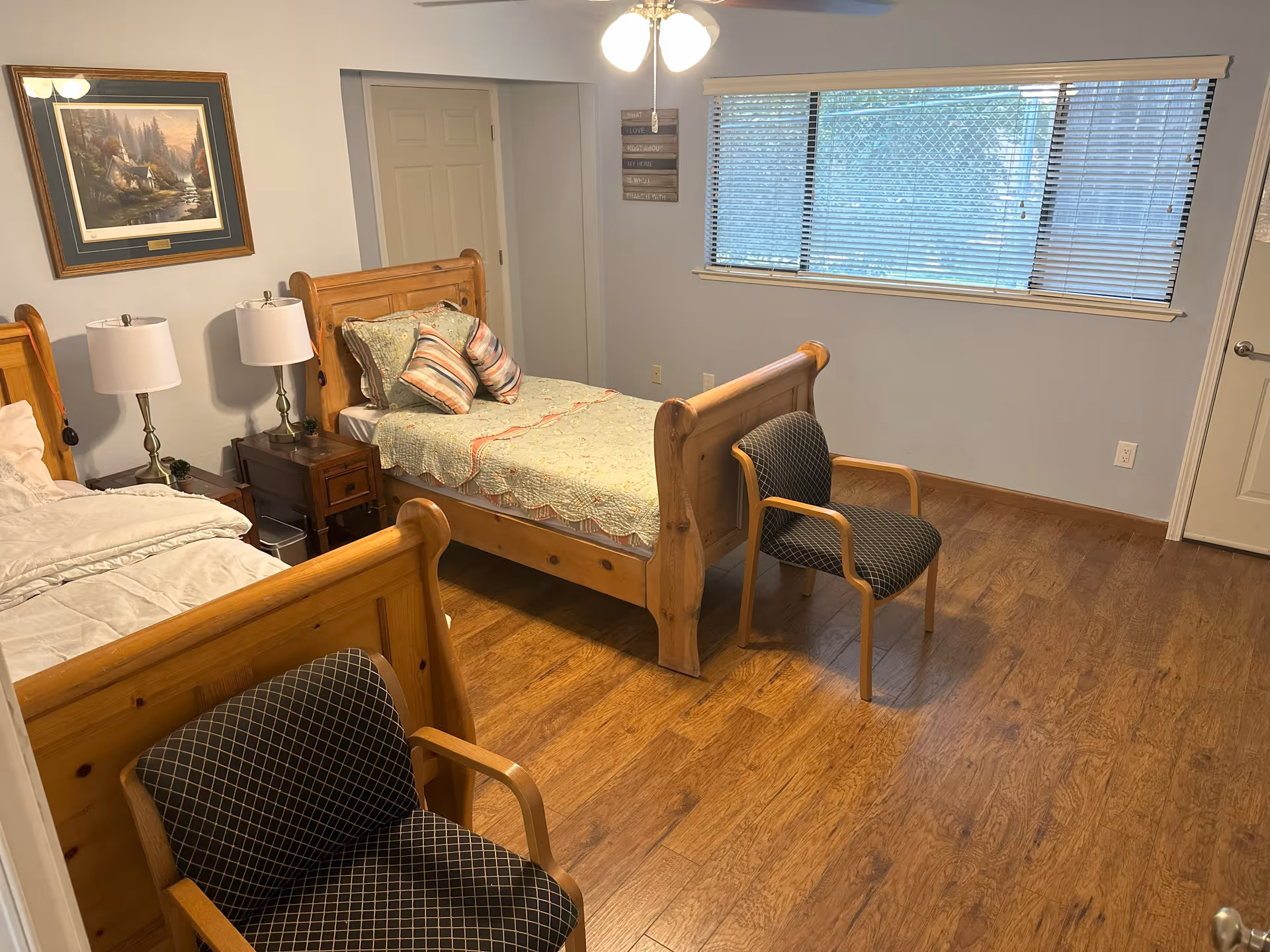 Two wooden twin beds with lamps, a chair, and windows in a cozy bedroom.