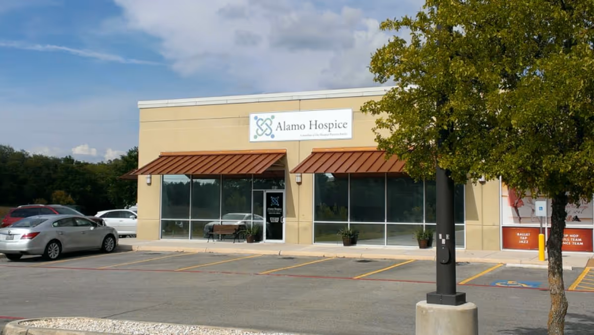 Front view of Alamo Hospice building with large windows and a parking lot.