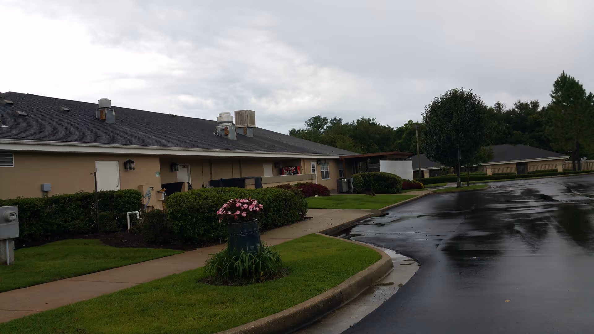 Exterior view of a single-story senior living facility with landscaping and a wet parking lot.