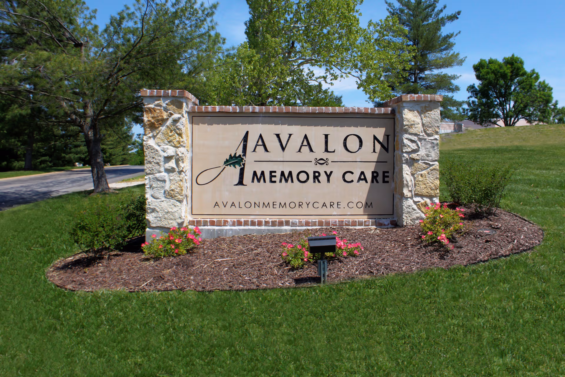 Stone Avalon Memory Care sign set in landscaped lawn with trees and shrubs.