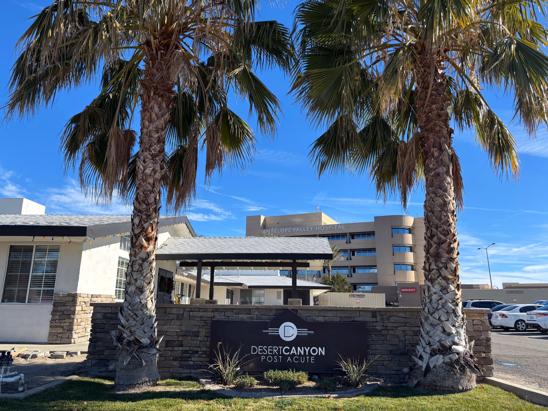 Exterior view of Desert Canyon Post Acute facility with palm trees and parking.