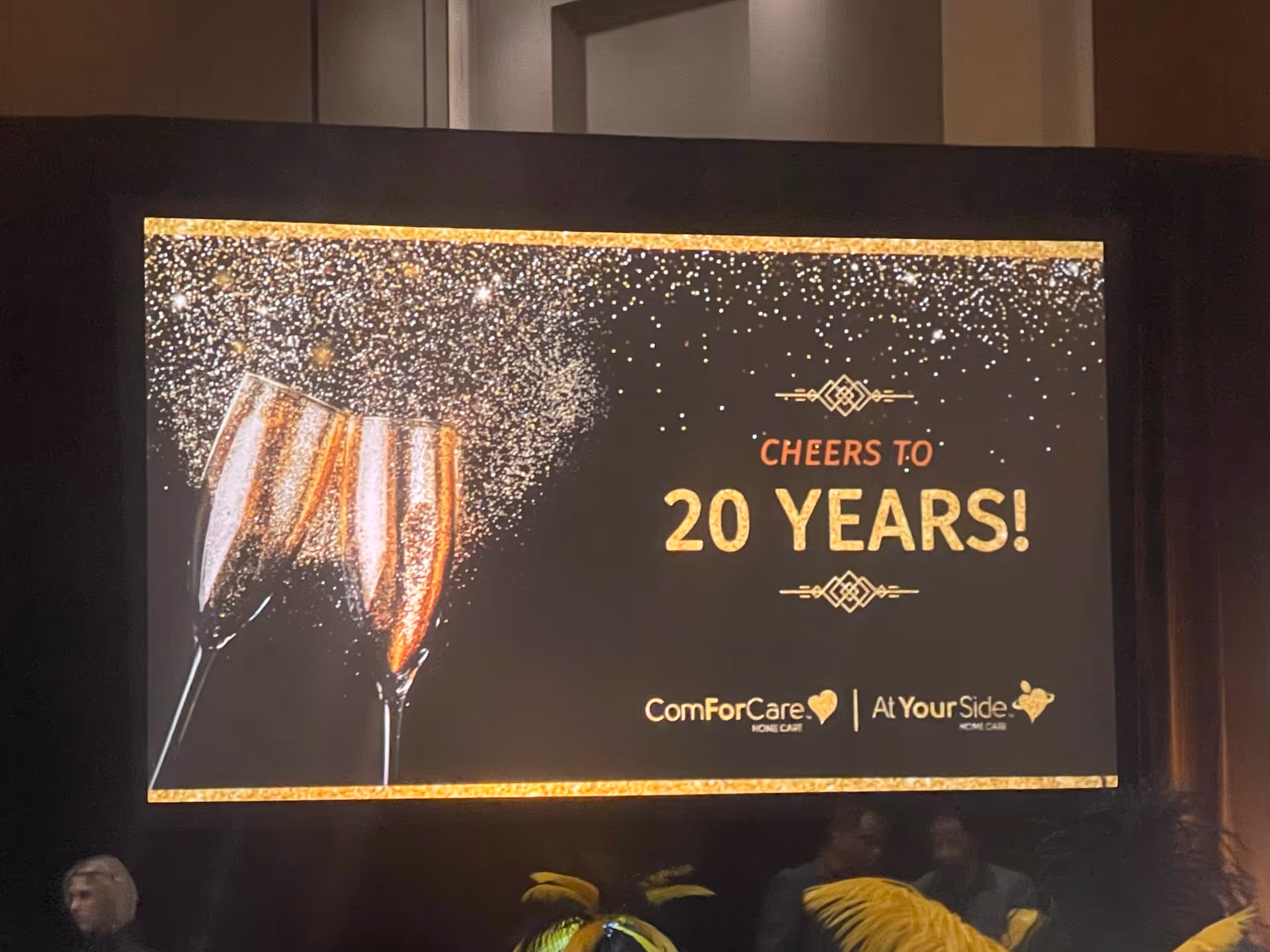 Indoor stage screen displaying Cheers to 20 Years with champagne glasses at a celebration.