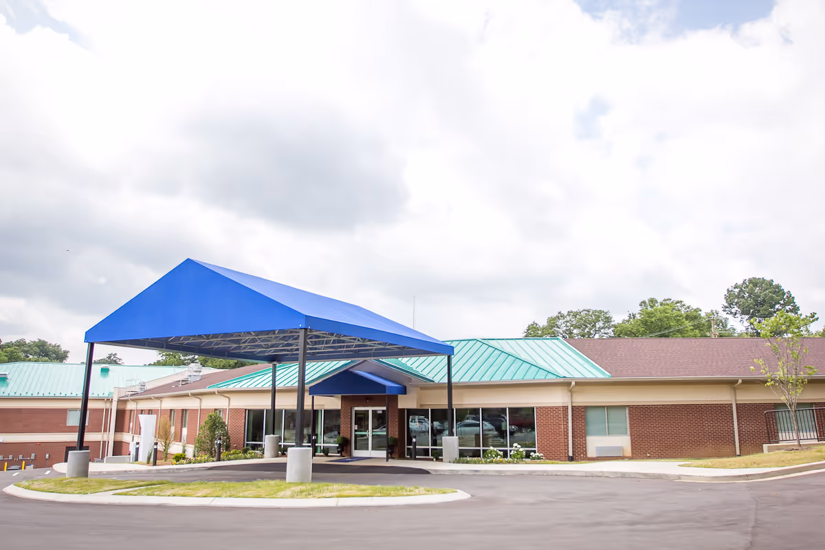 Brick senior living facility exterior with a blue entry canopy and green roof.