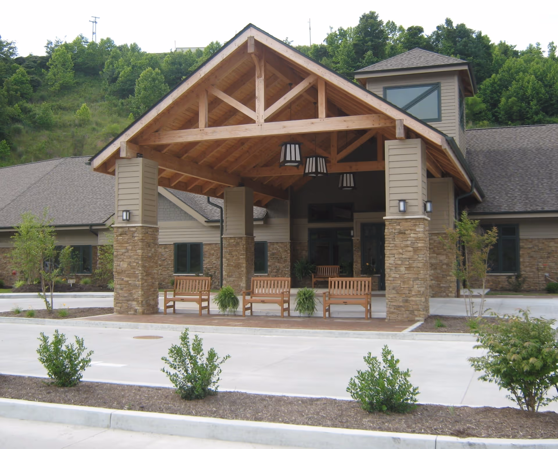 Front entrance of a senior care facility with stone pillars, wooden beams, and benches.