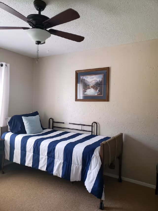 Bedroom in Ontiveros Foster Home with striped blue-and-white bed, ceiling fan, and wall art.