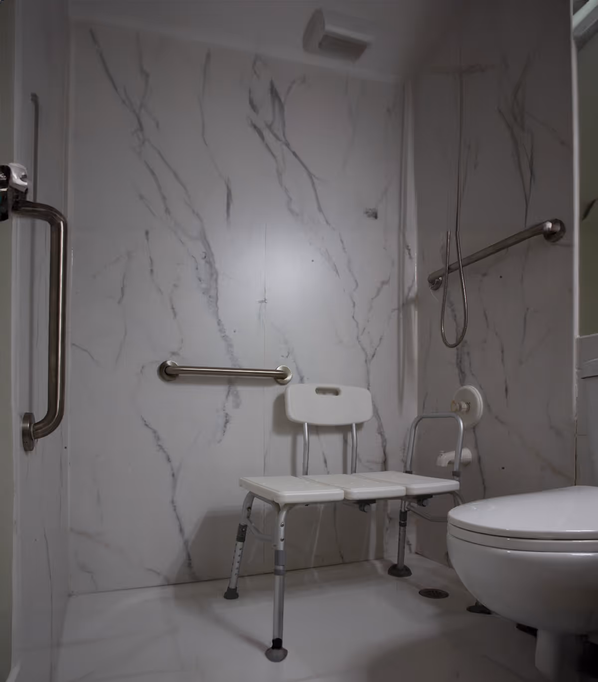 Accessible bathroom with marble walls, a shower chair, grab bars, and a toilet.