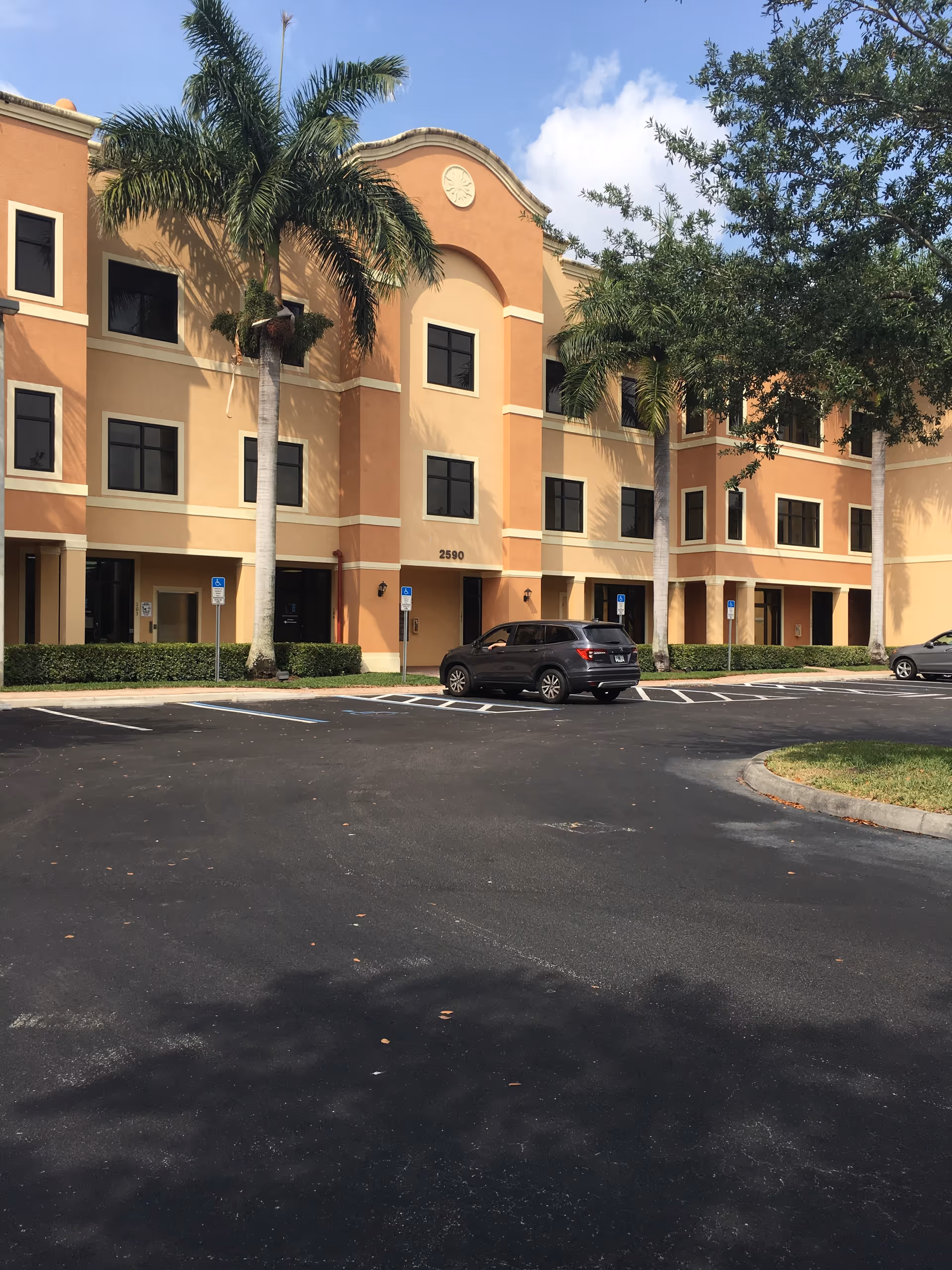Exterior view of a peach-colored senior living building with palm trees and a parking lot.