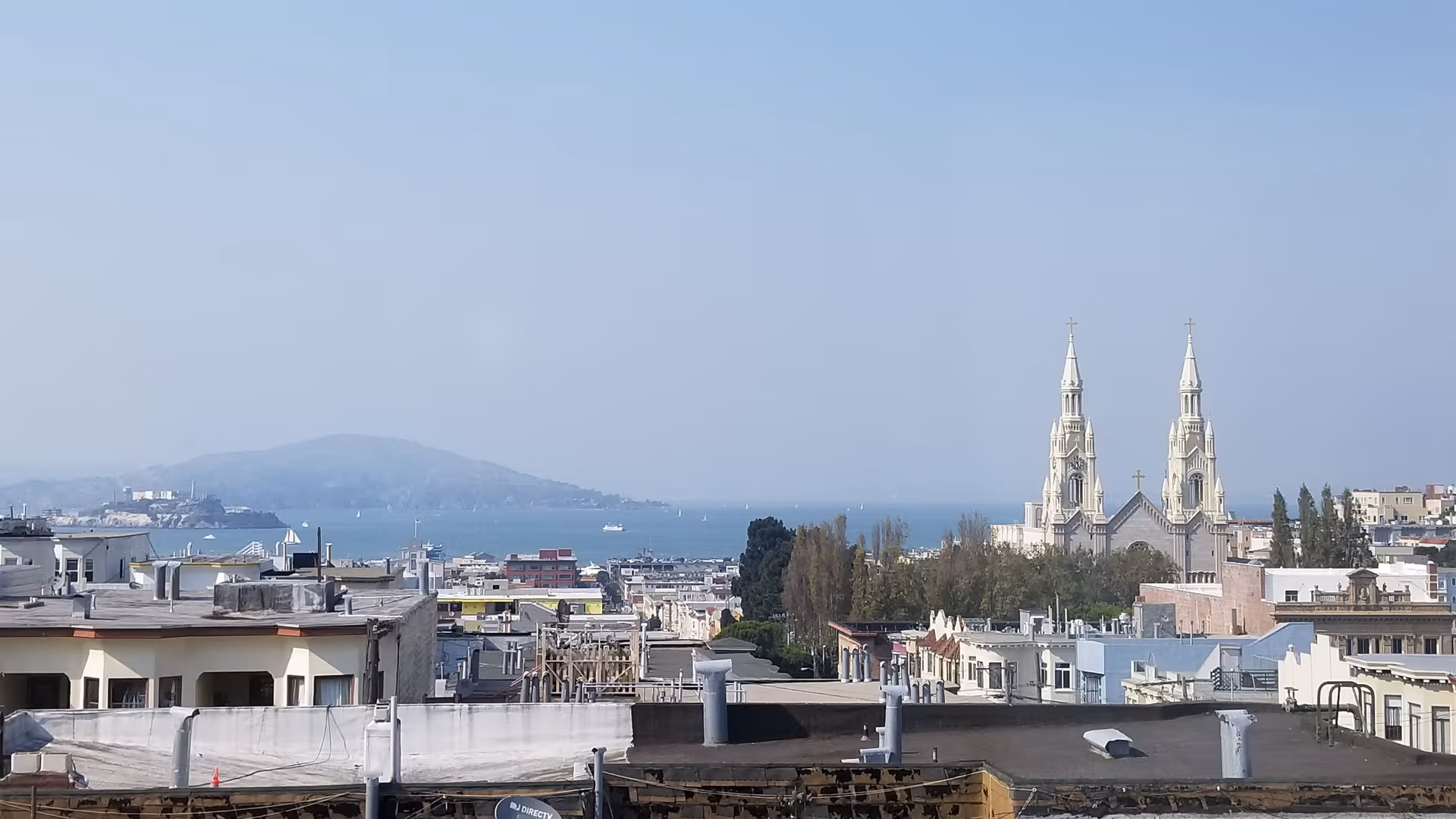City skyline with rooftops, a distant bay, and twin church towers.