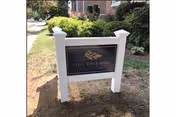 Outdoor white-framed sign with a dark plaque reading Lydia H. Roper Home beside a sidewalk.