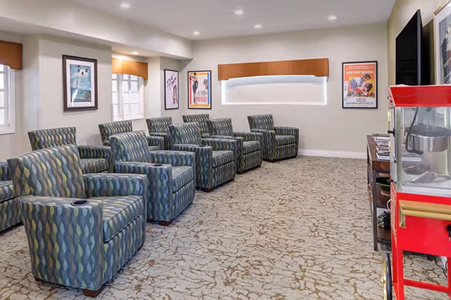 Spacious senior living lounge with blue patterned chairs and a red popcorn cart.