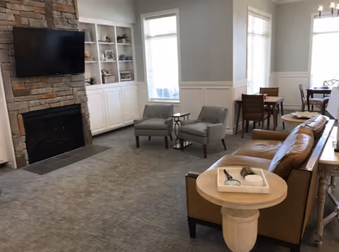 Cozy living room at Adams County Nursing Center with fireplace, shelves, chairs, sofa, and dining area.