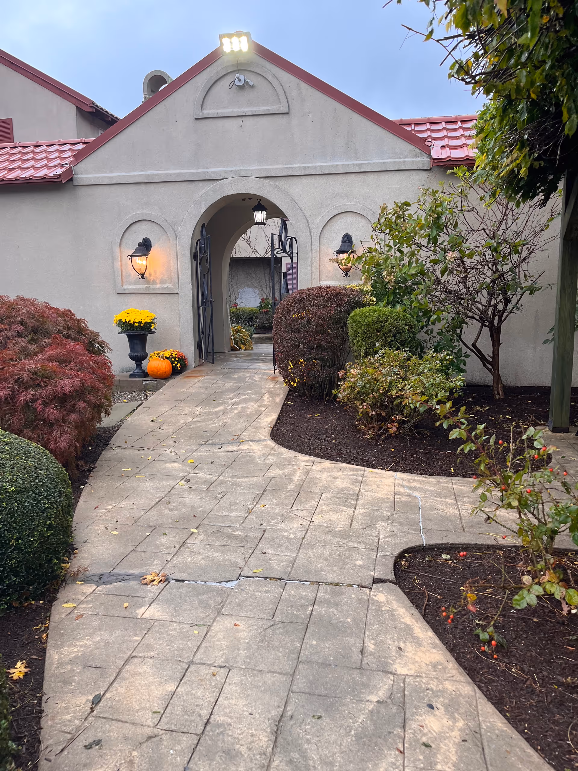 Entrance walkway to a senior facility with an arched doorway and autumn landscaping.
