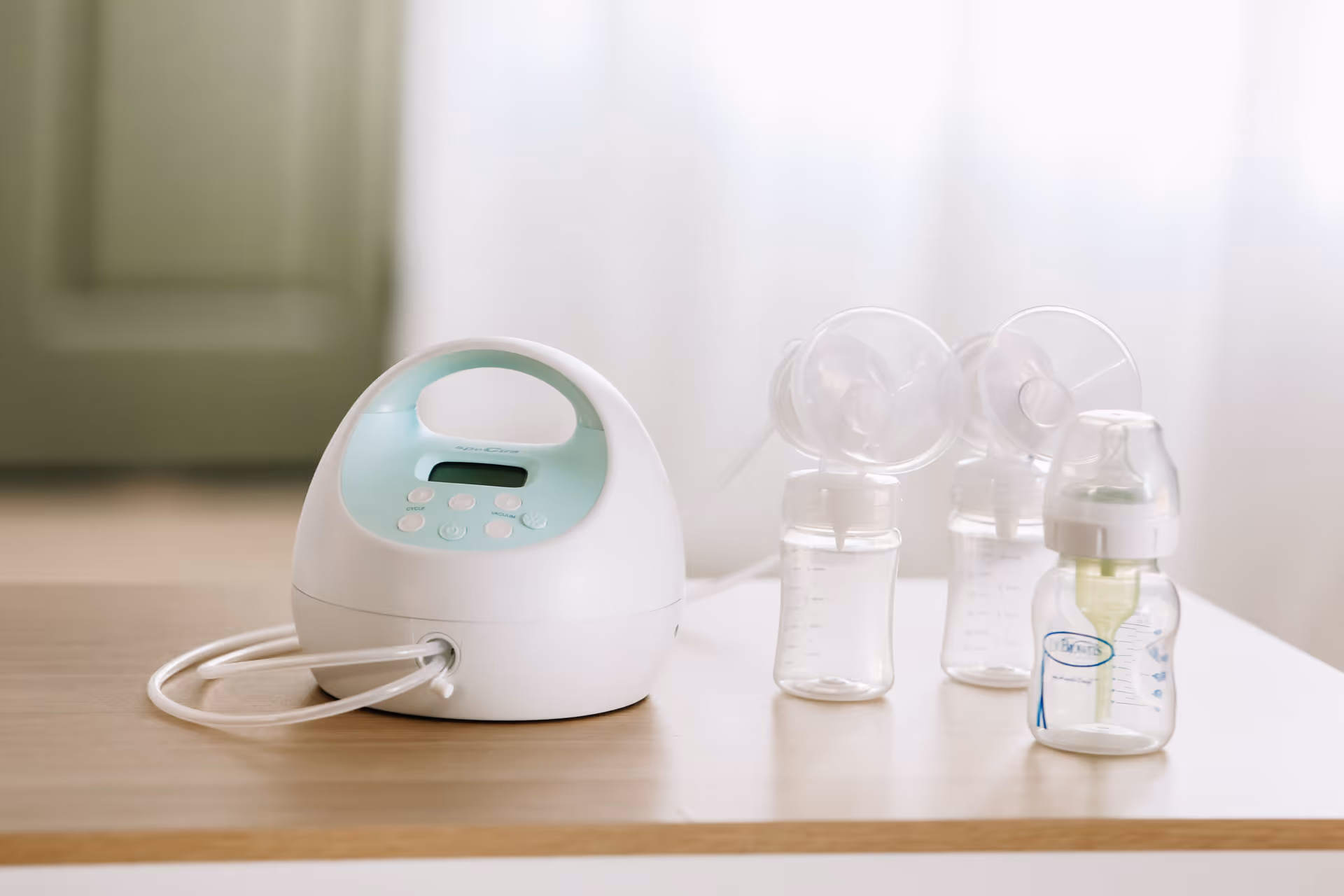 Breast pump with bottles sits on a wooden table in a softly lit room