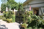 Front exterior of Westchester Gardens featuring a gate, walkway, and lush greenery.