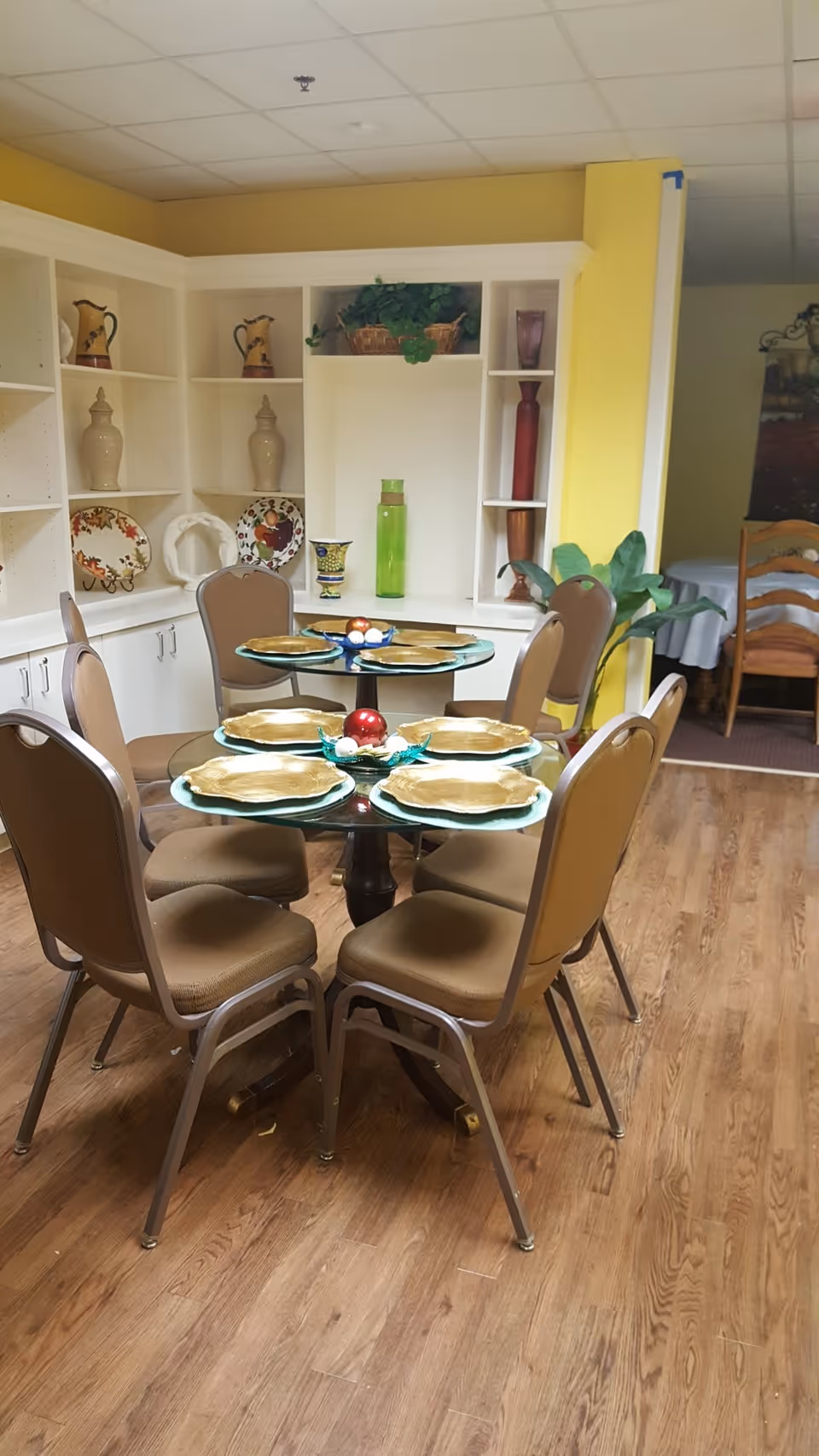 Round glass dining table with six beige chairs in a bright yellow dining room.
