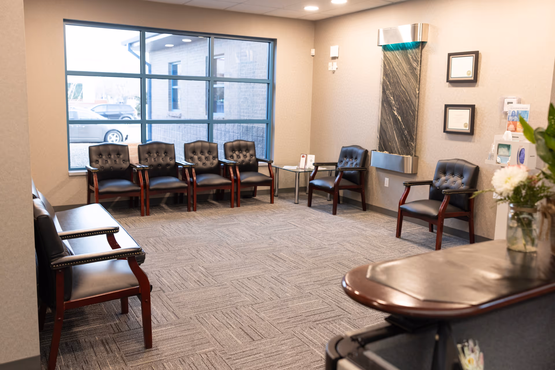 Spacious beige-walled indoor waiting area with black cushioned chairs and a reception desk.