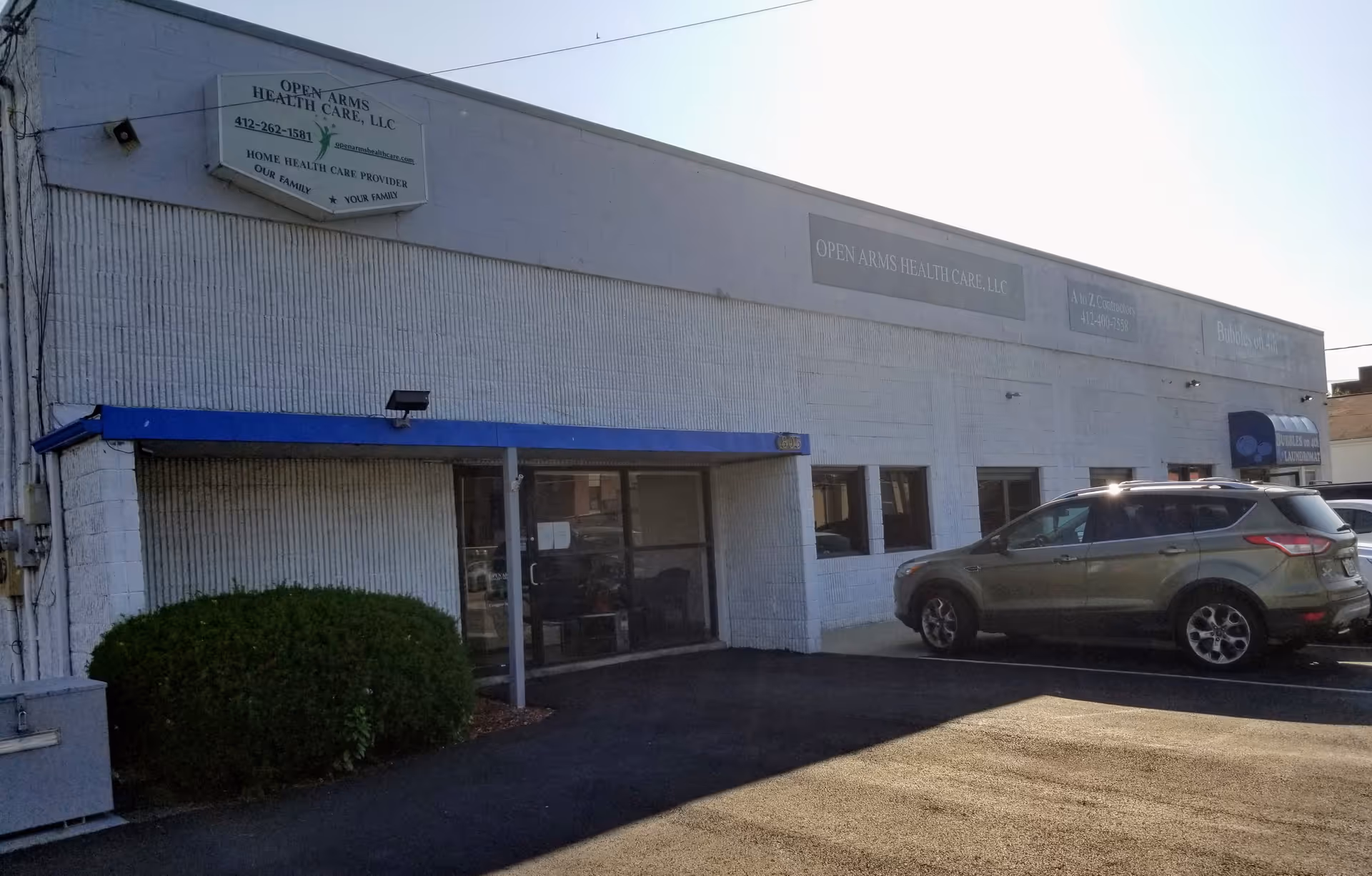White commercial building with Open Arms Health Care signage and a parked SUV.