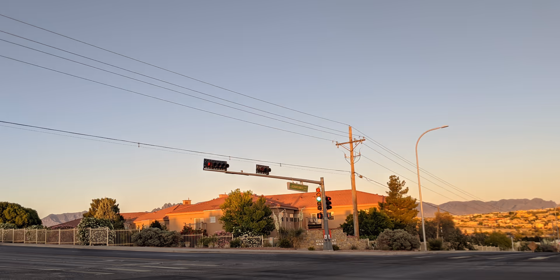 Sunlit exterior view of a senior living building with a fence and desert landscape.