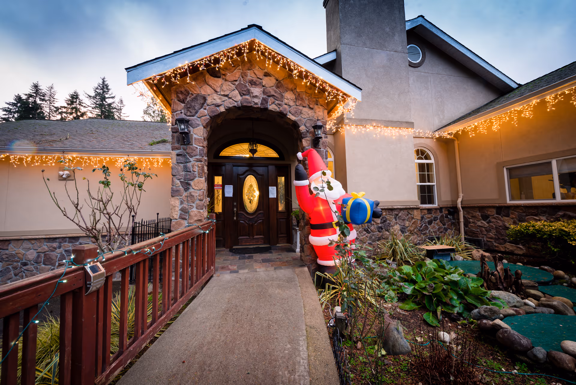 Exterior view of the facility entrance with stone arch, festive lights, and a garden.