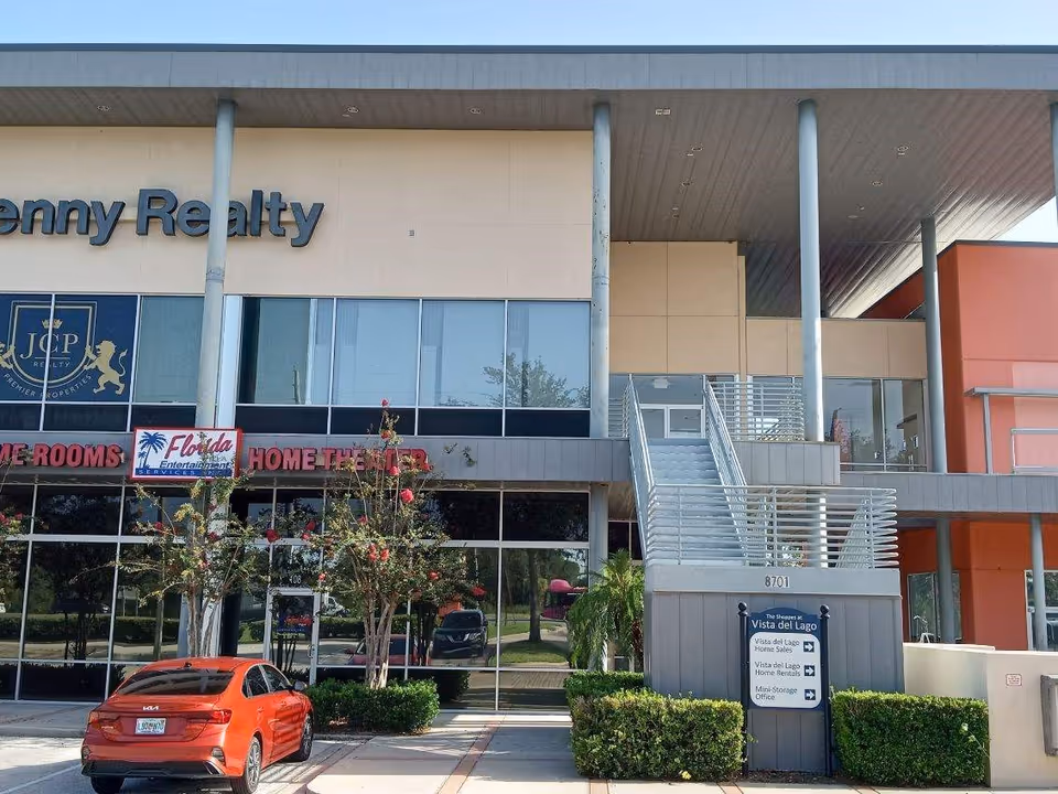 Modern two-story commercial building with large glass windows and a metal staircase, parking lot in front.