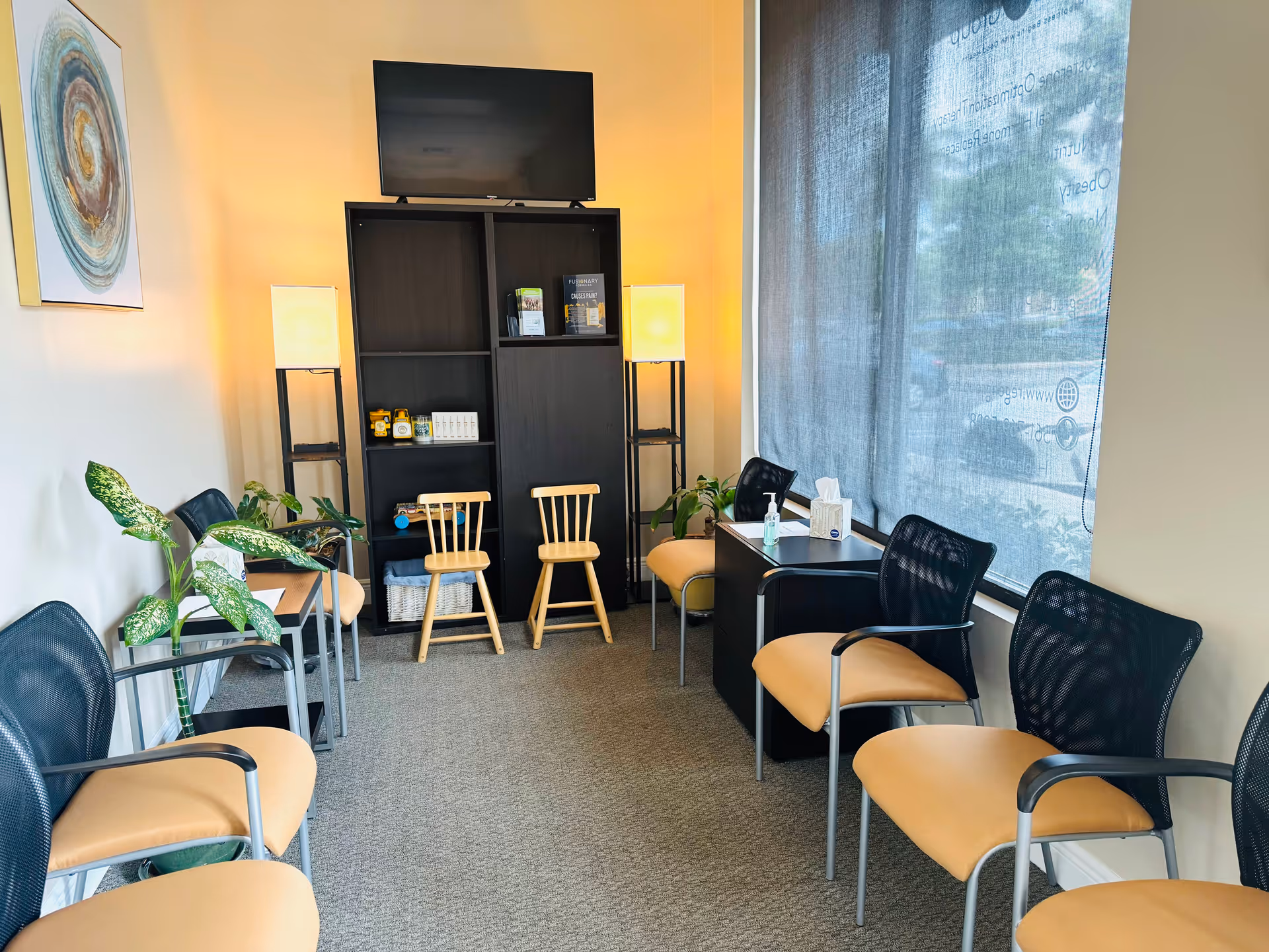 A cozy interior lounge in a senior facility with beige chairs, plants, and shelving.
