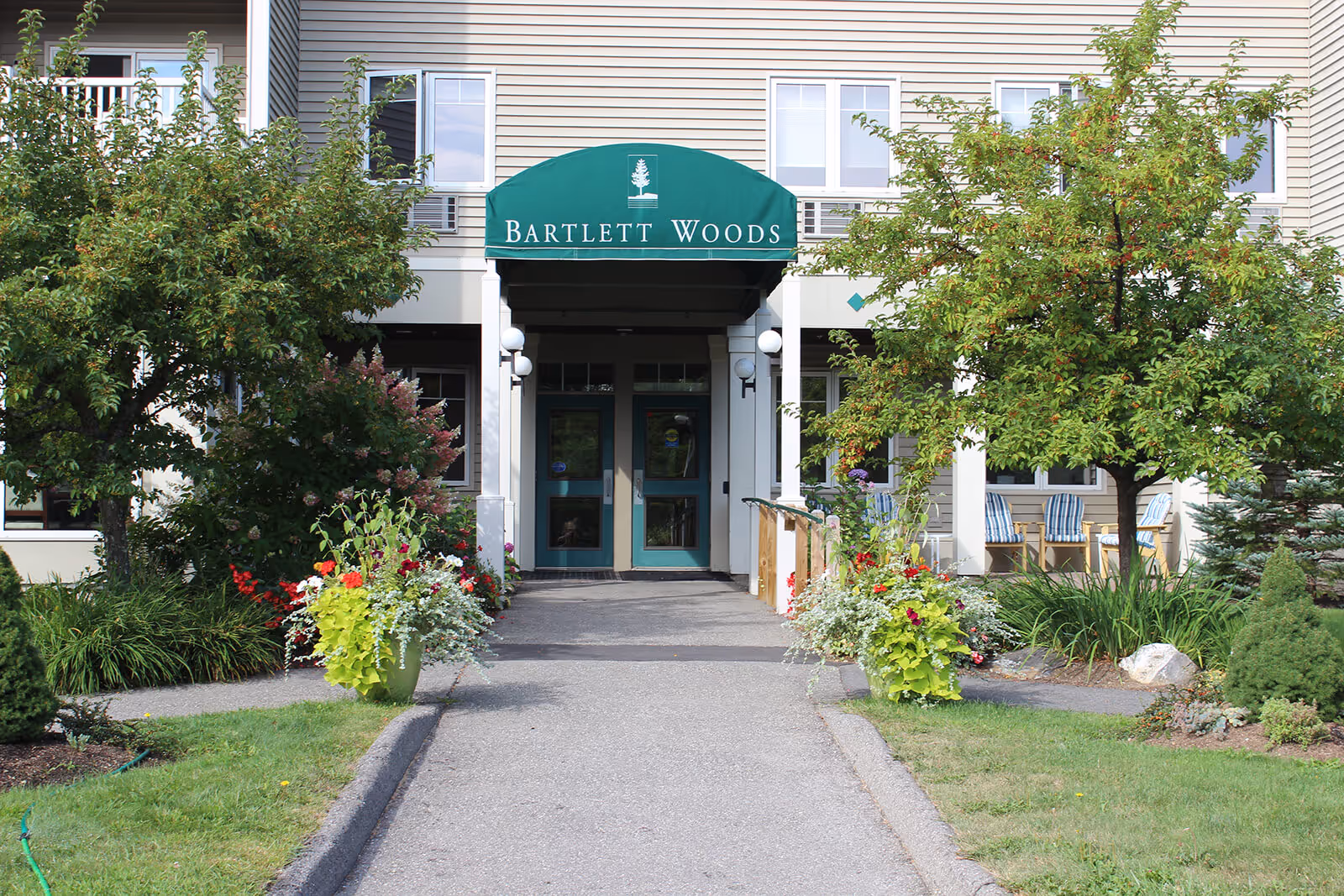 Front entrance of the Bartlett Woods building with a green awning, double doors, and a landscaped walkway.
