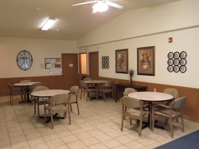 Interior dining room with round tables, beige chairs, and wall decor in a senior facility.