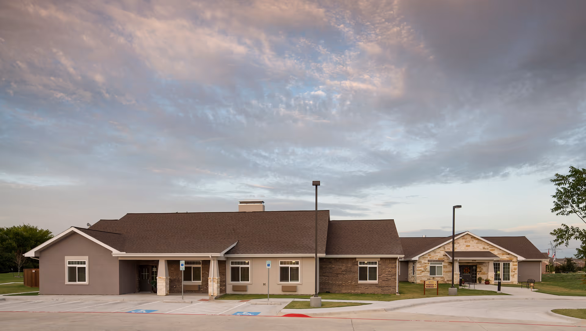 Single-story memory care facility exterior with parking, entrances, and varied stone accents.