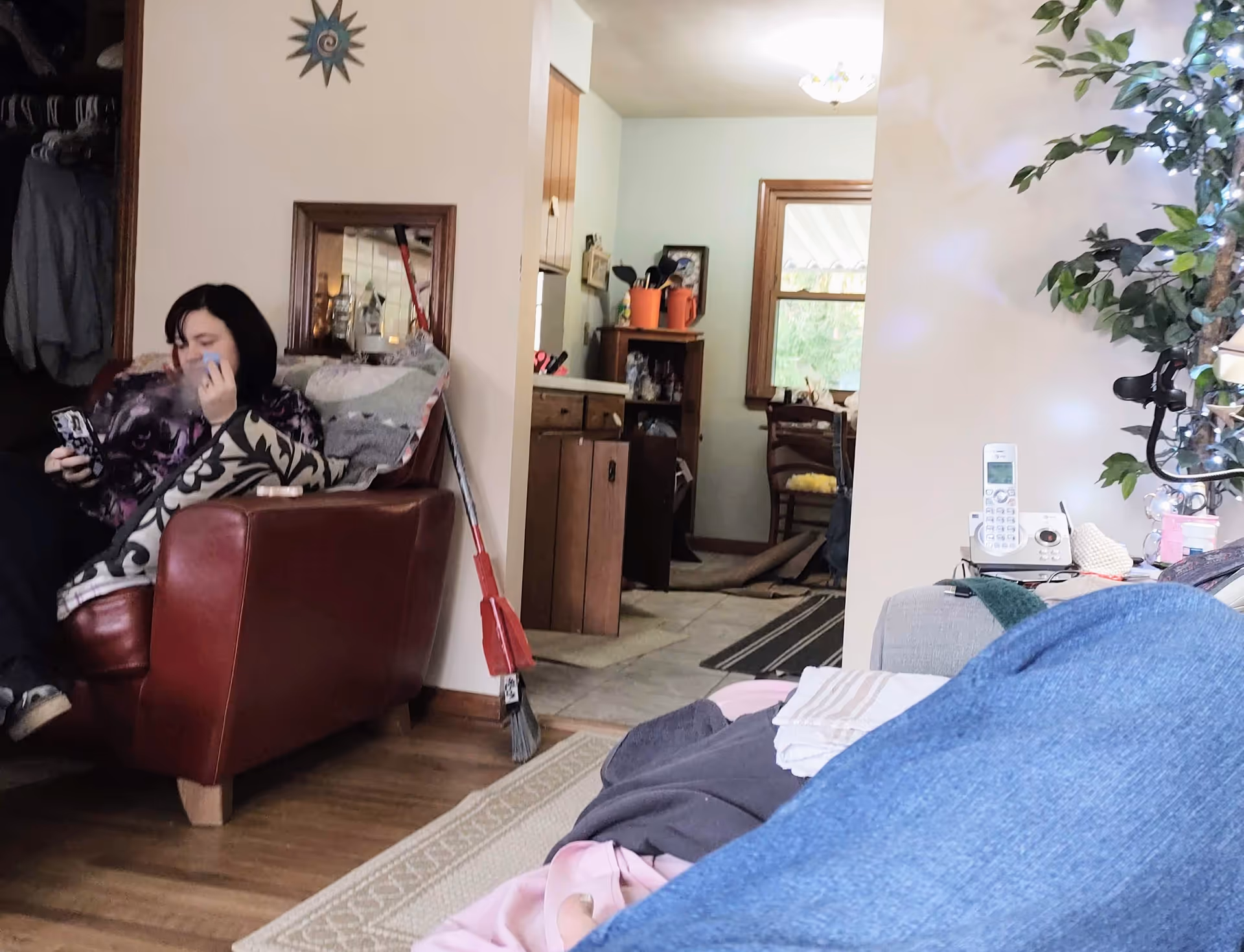 Woman seated in a red armchair in a cozy living room with a broom nearby.