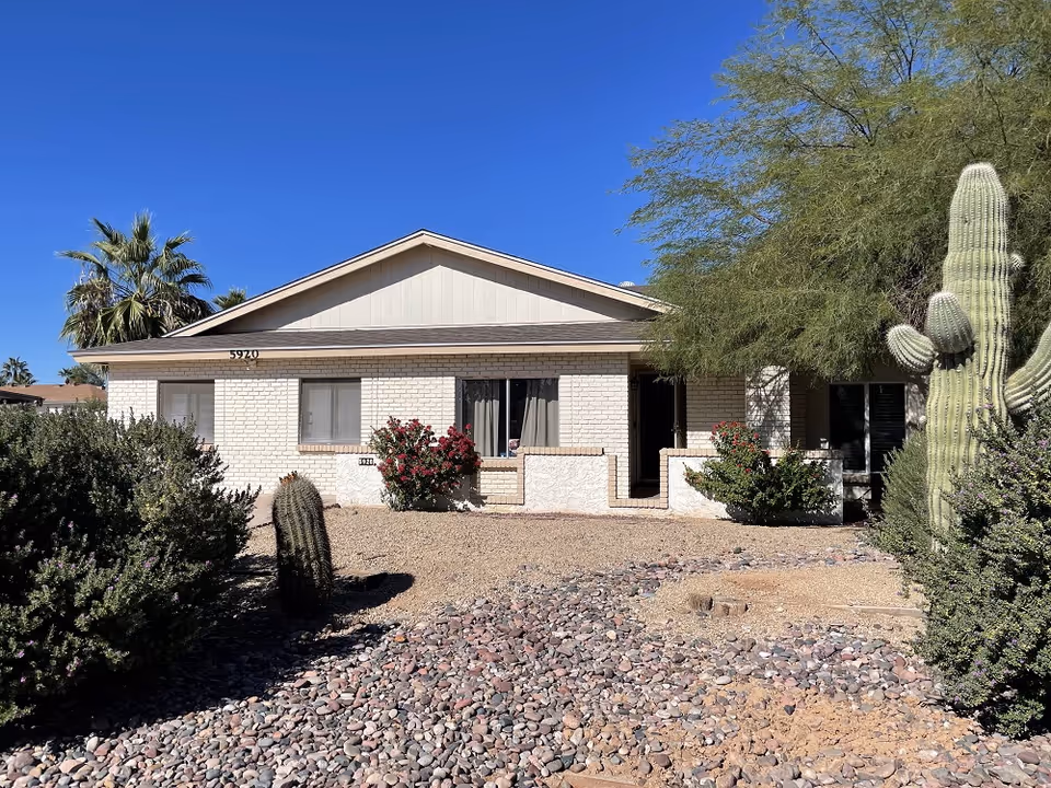 Front view of a single-story beige brick care home with desert landscaping.