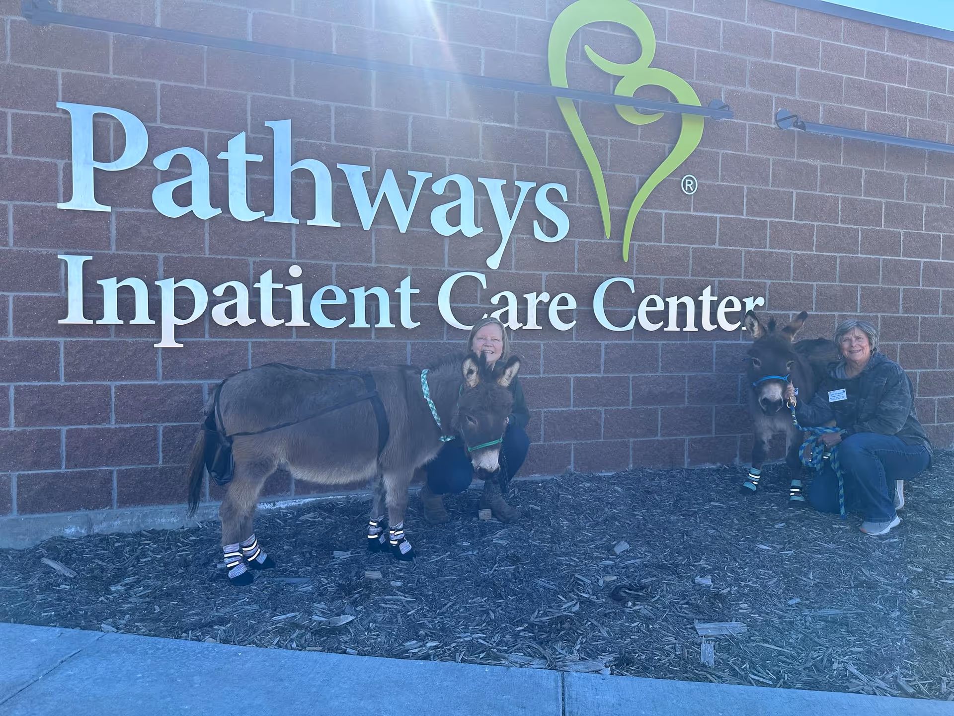 Outside Pathways Inpatient Care Center, two people pose with two ponies by the building.