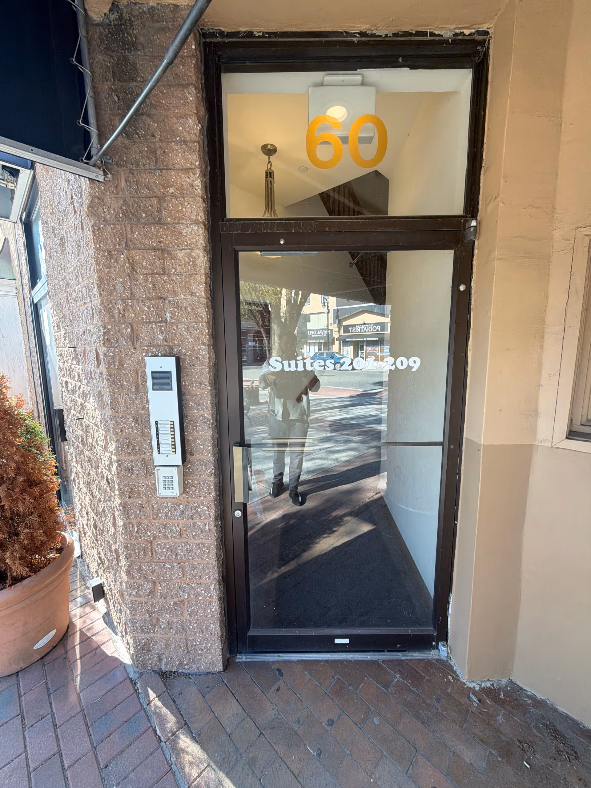 Front entrance of the facility with a glass door labeled Suites 201-209 and brick exterior.