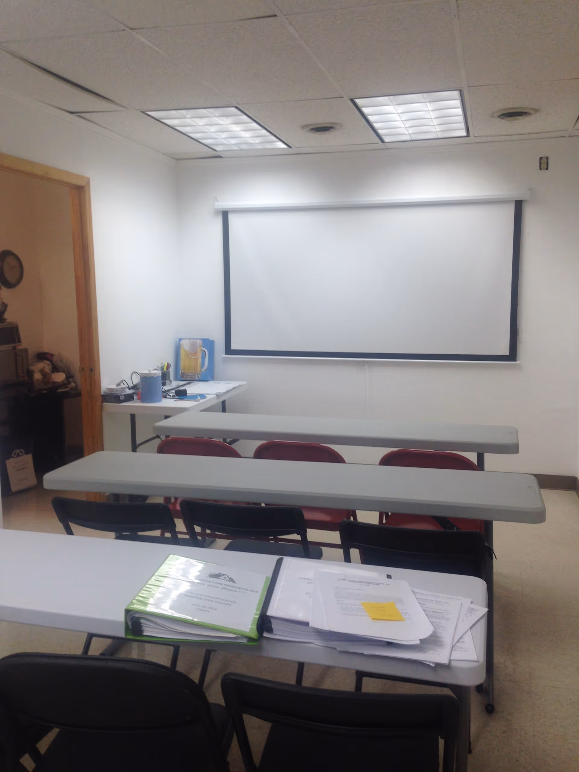 Small training room with desks, folding chairs, and a projection screen at front.