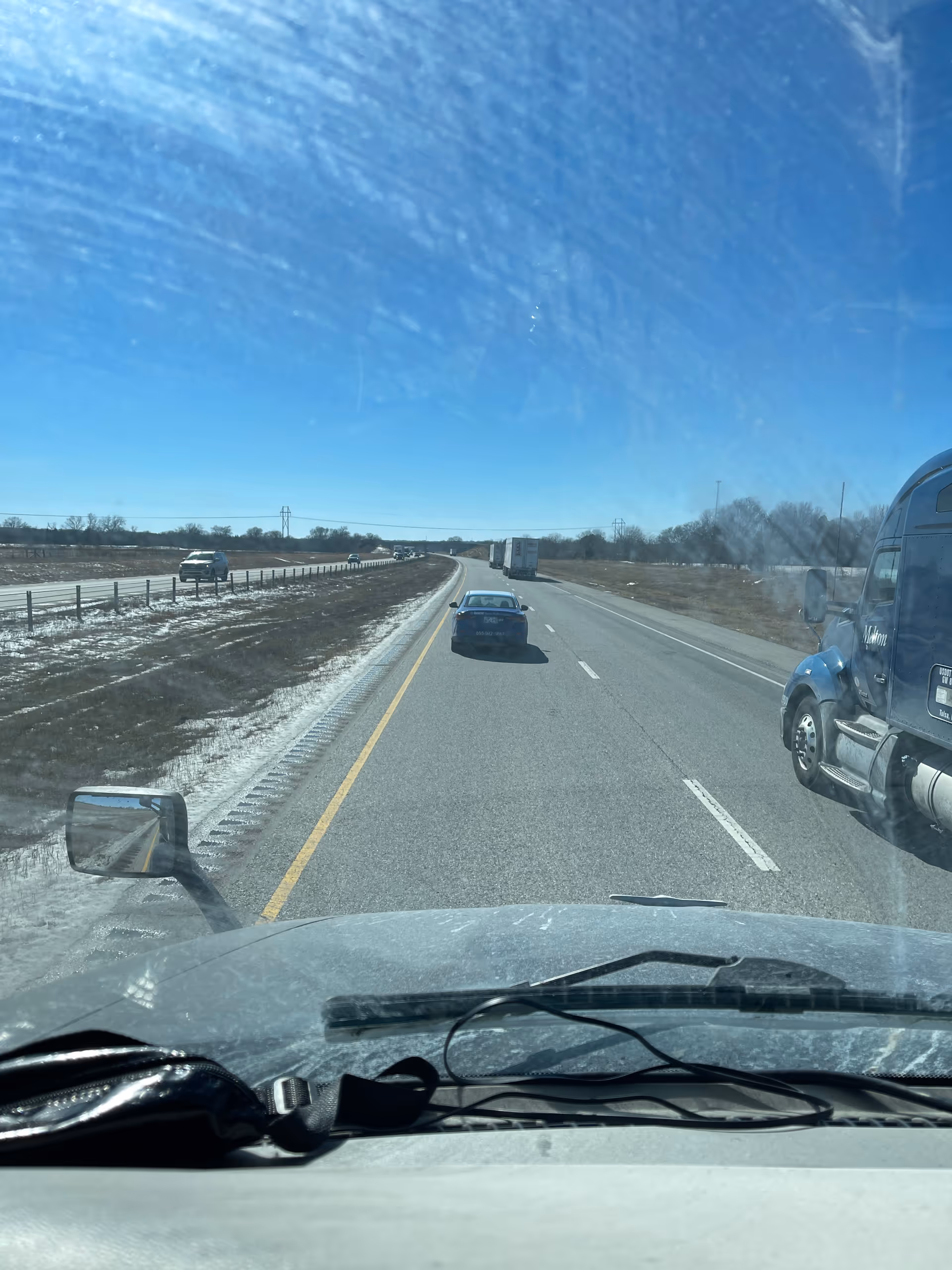 Driver's view of highway ahead with trucks and barren landscape on a sunny day