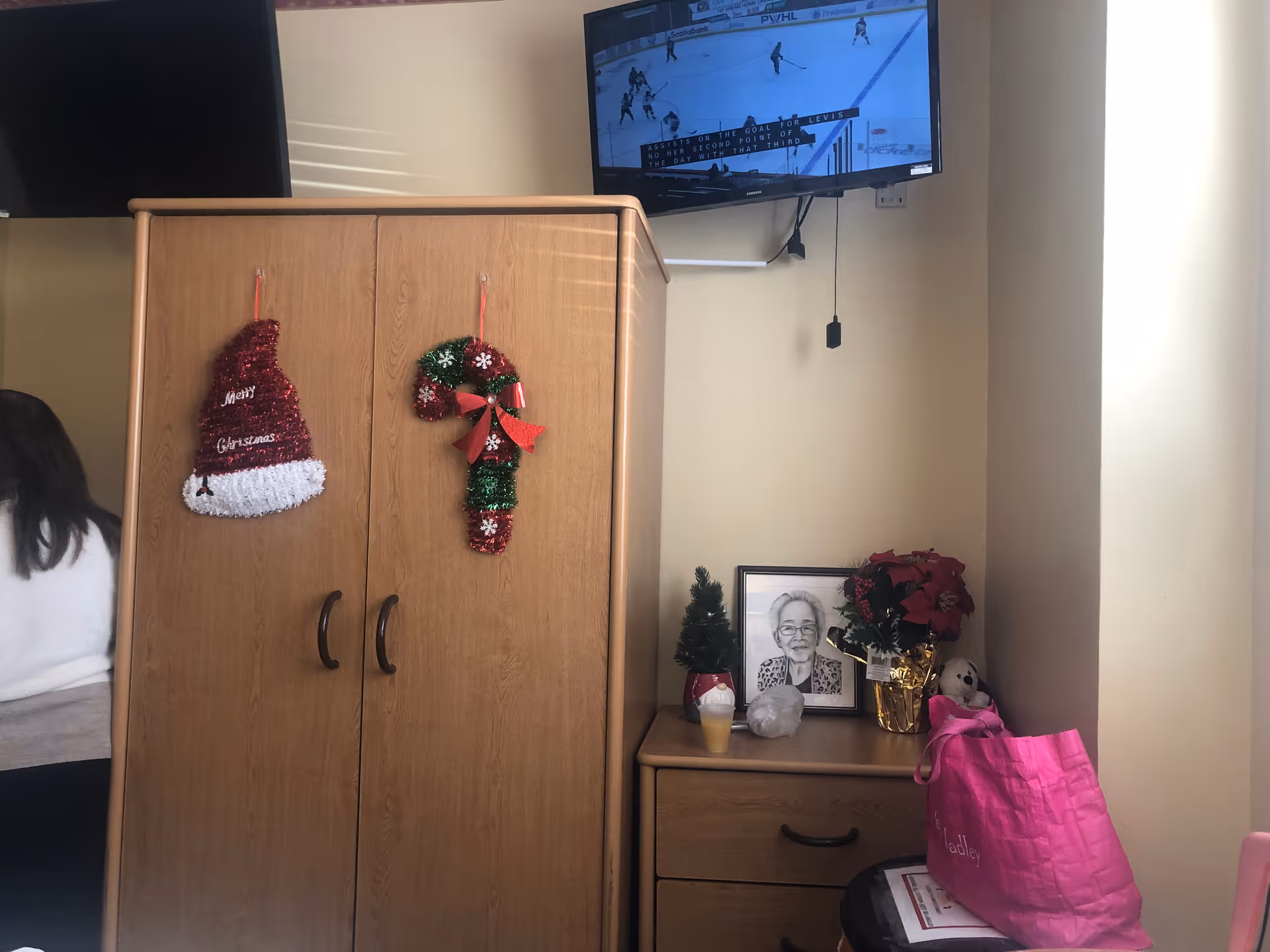 Wooden cabinet with Christmas stockings, decorations, a dresser, and a mounted TV in a cozy room.
