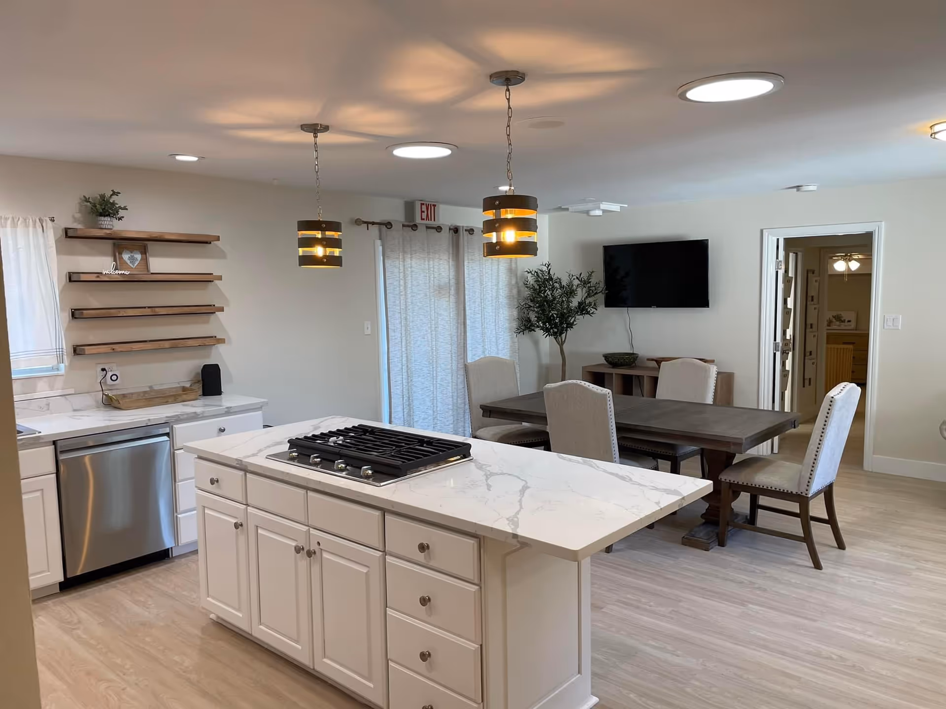Open kitchen with marble island, dining table, and wall-mounted TV in a senior living home.