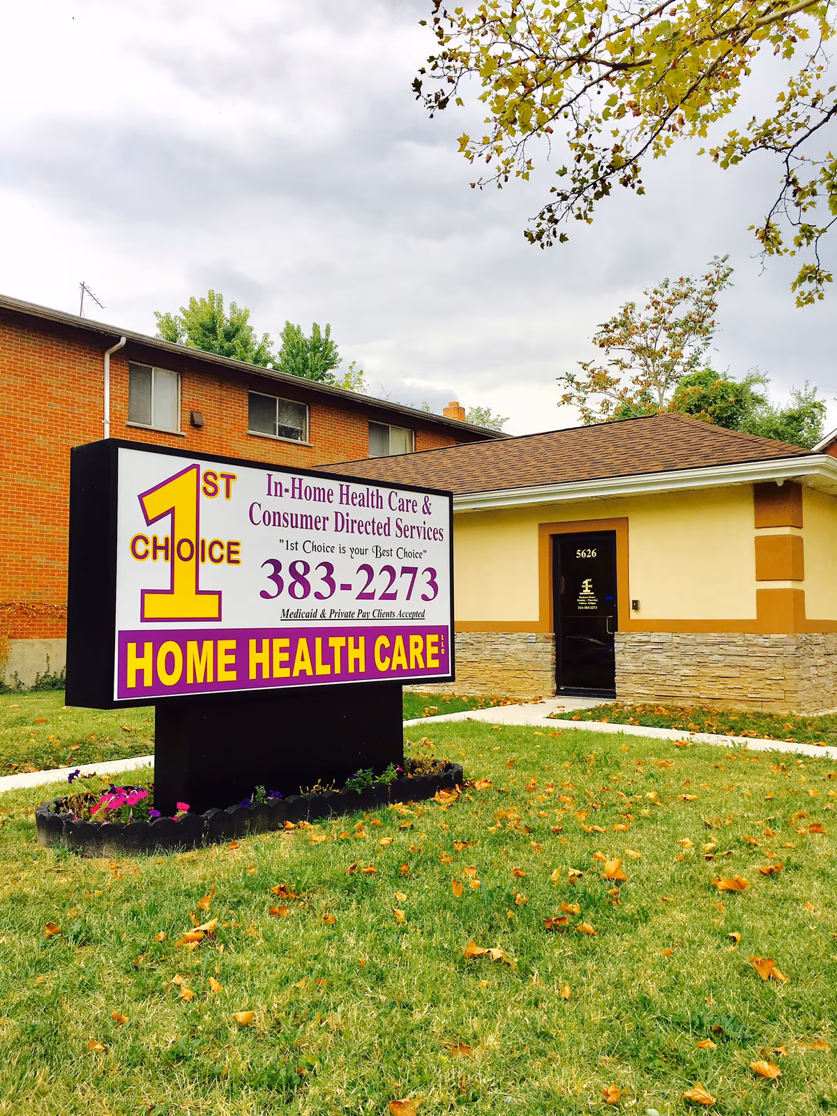A large sign for 1st Choice Home Health Care in front of a brick building.