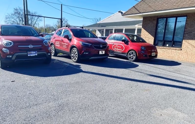 Red Home Helpers vehicles parked in front of a brick facility entrance.