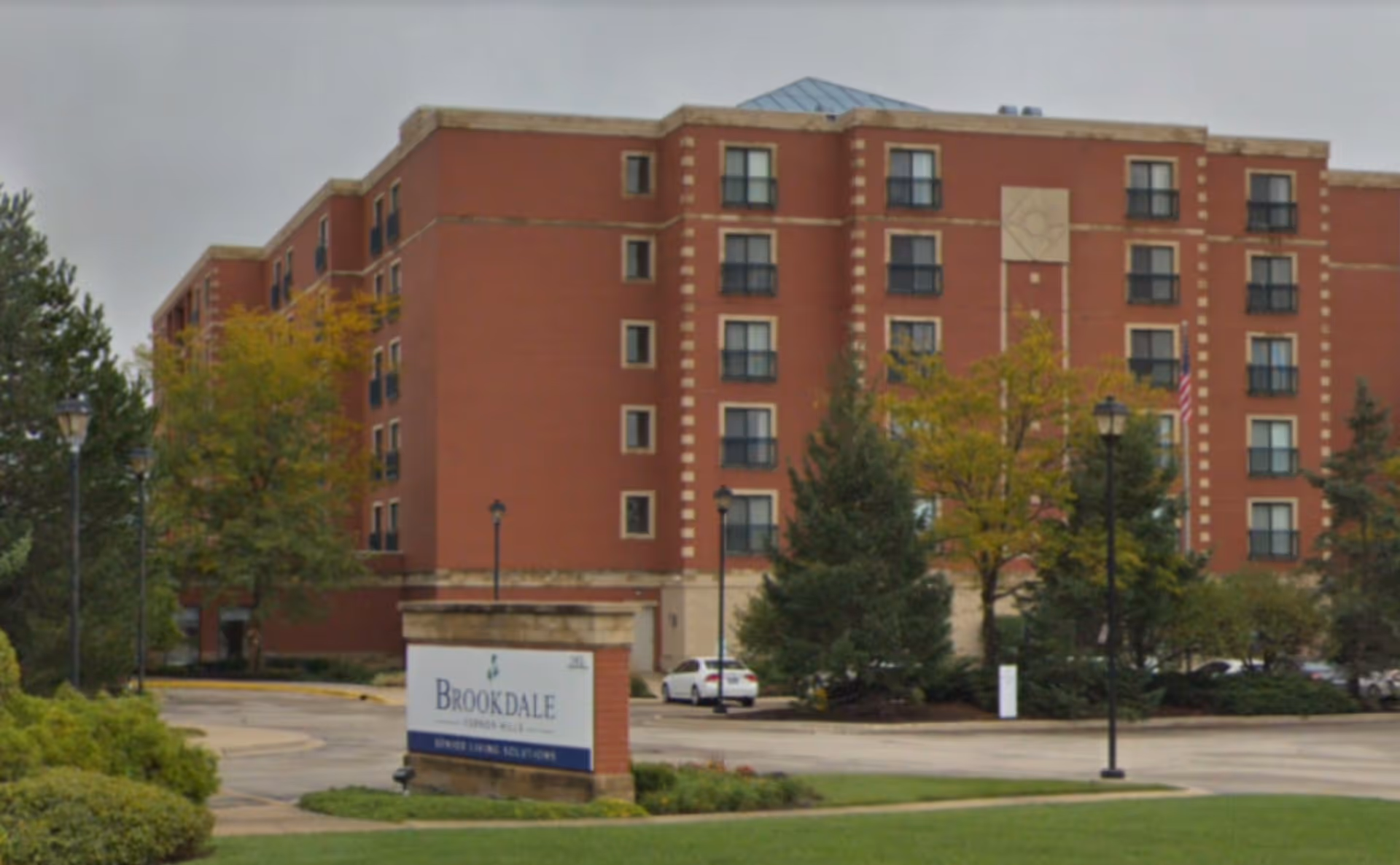 Brick senior living building with Brookdale sign, trees, and a parking lot.