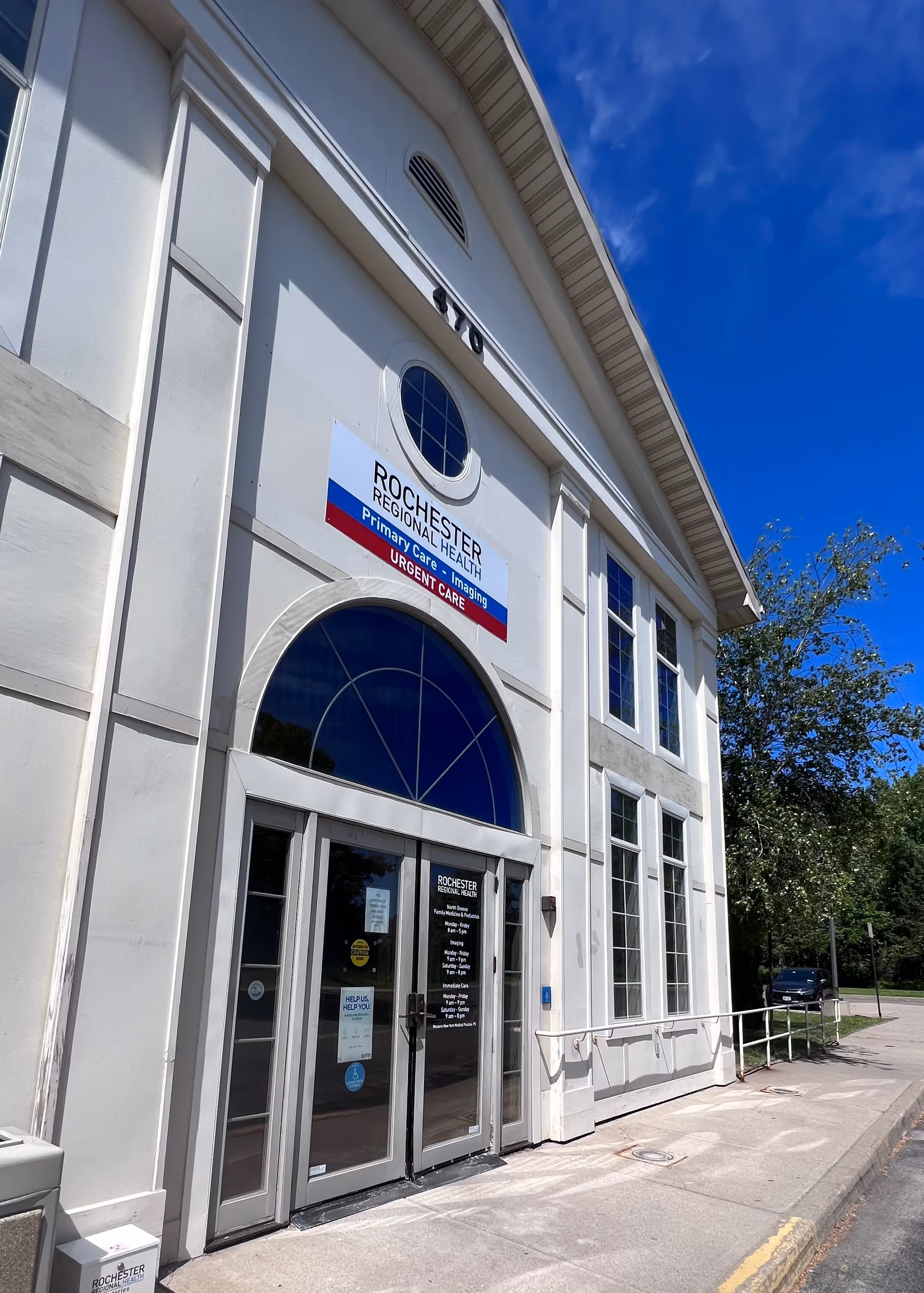 White medical facility front with arched blue window above glass entrance doors.