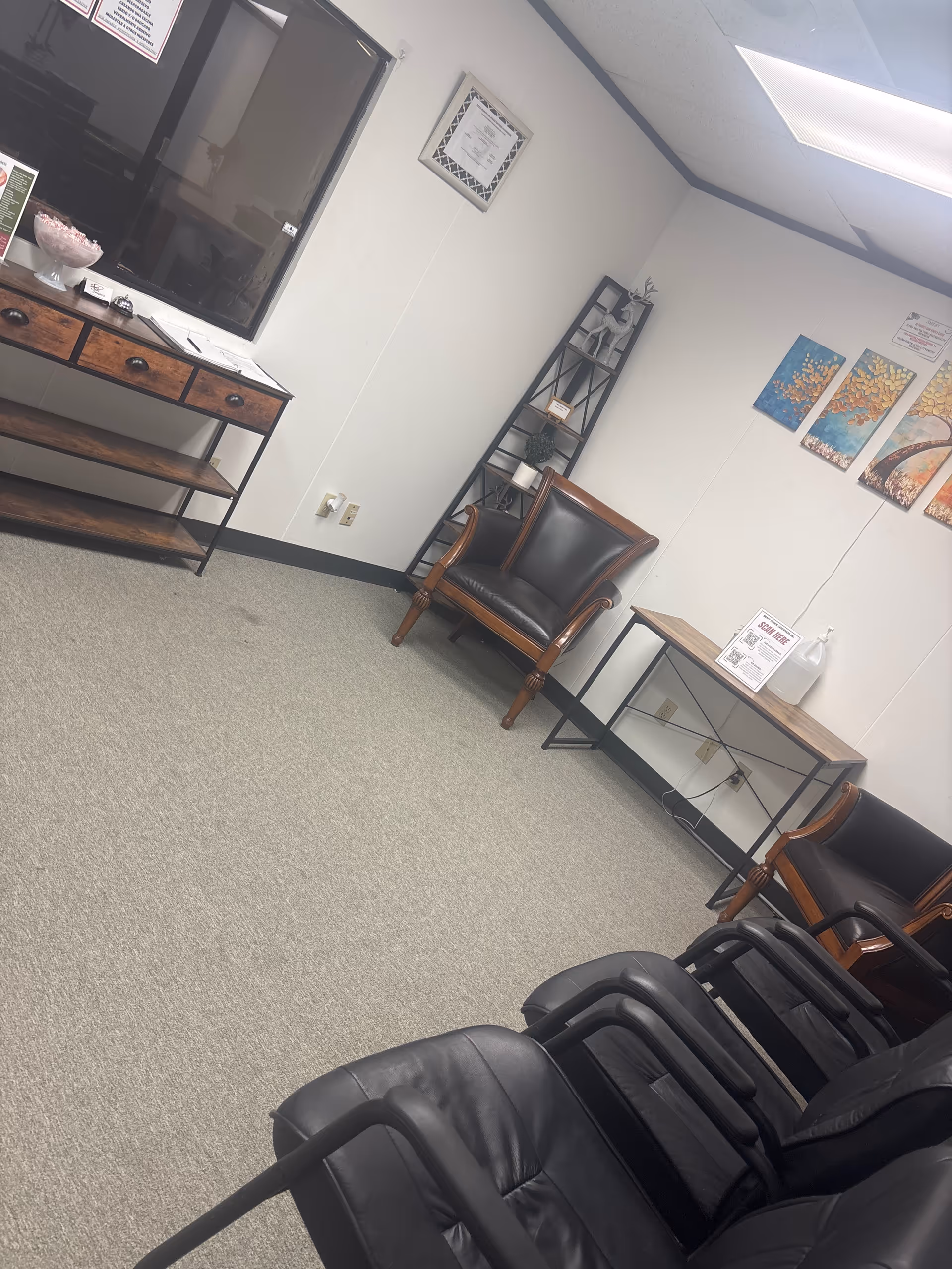 Interior waiting area with black leather chairs, tables, shelves, and wall art.