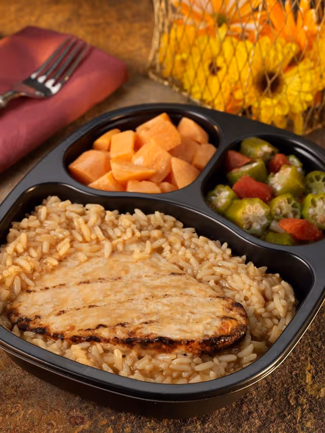 Segmented meal tray with chicken, rice, and mixed vegetables on a table.