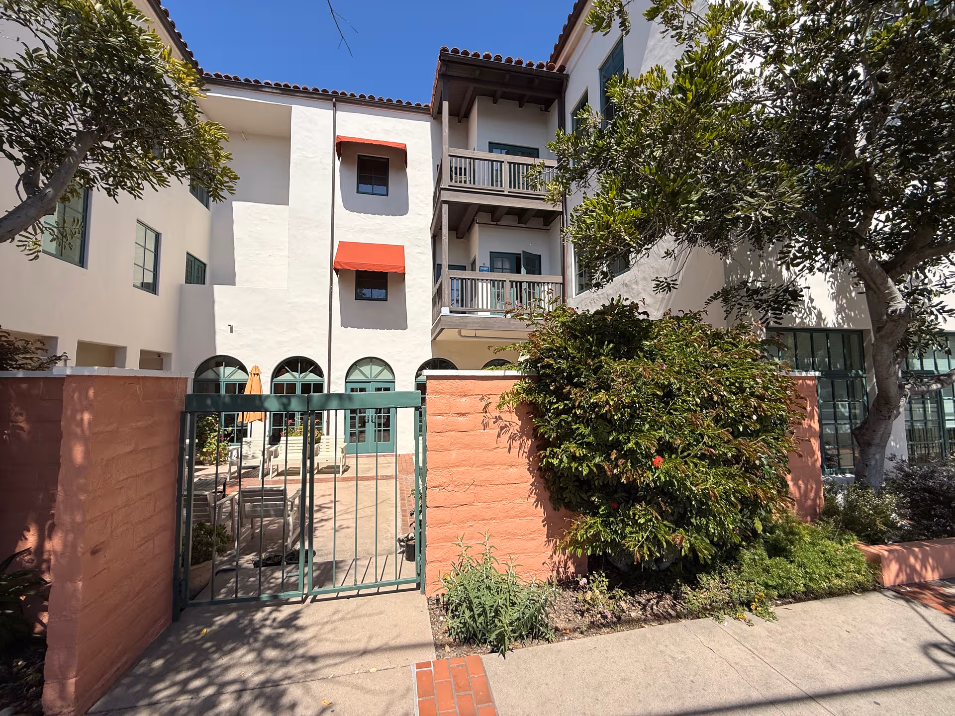 Stucco building exterior with arches, balconies, and a green gate in a landscaped courtyard.