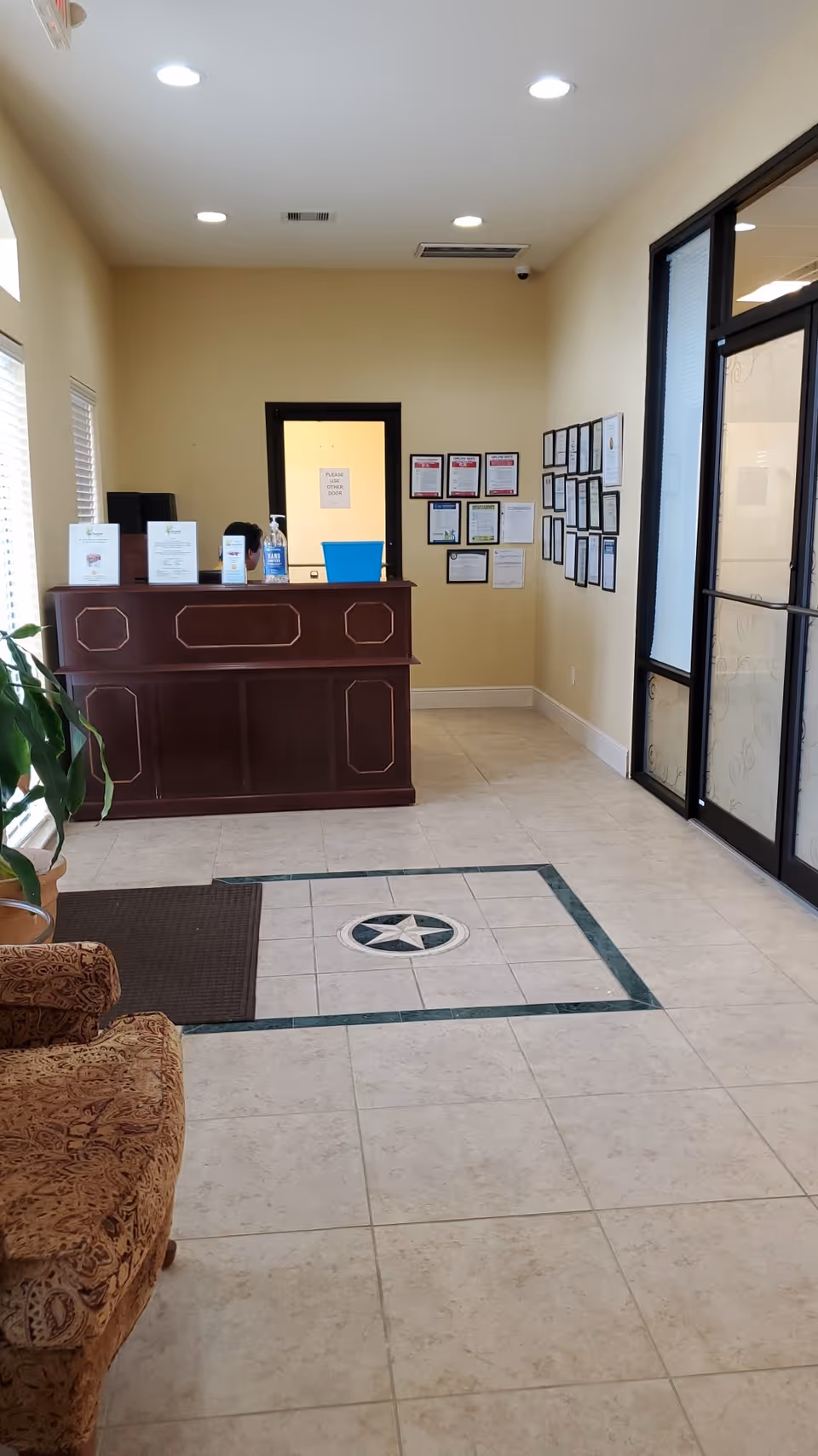 Reception desk in a beige-toned lobby with certificates on the wall and glass doors.