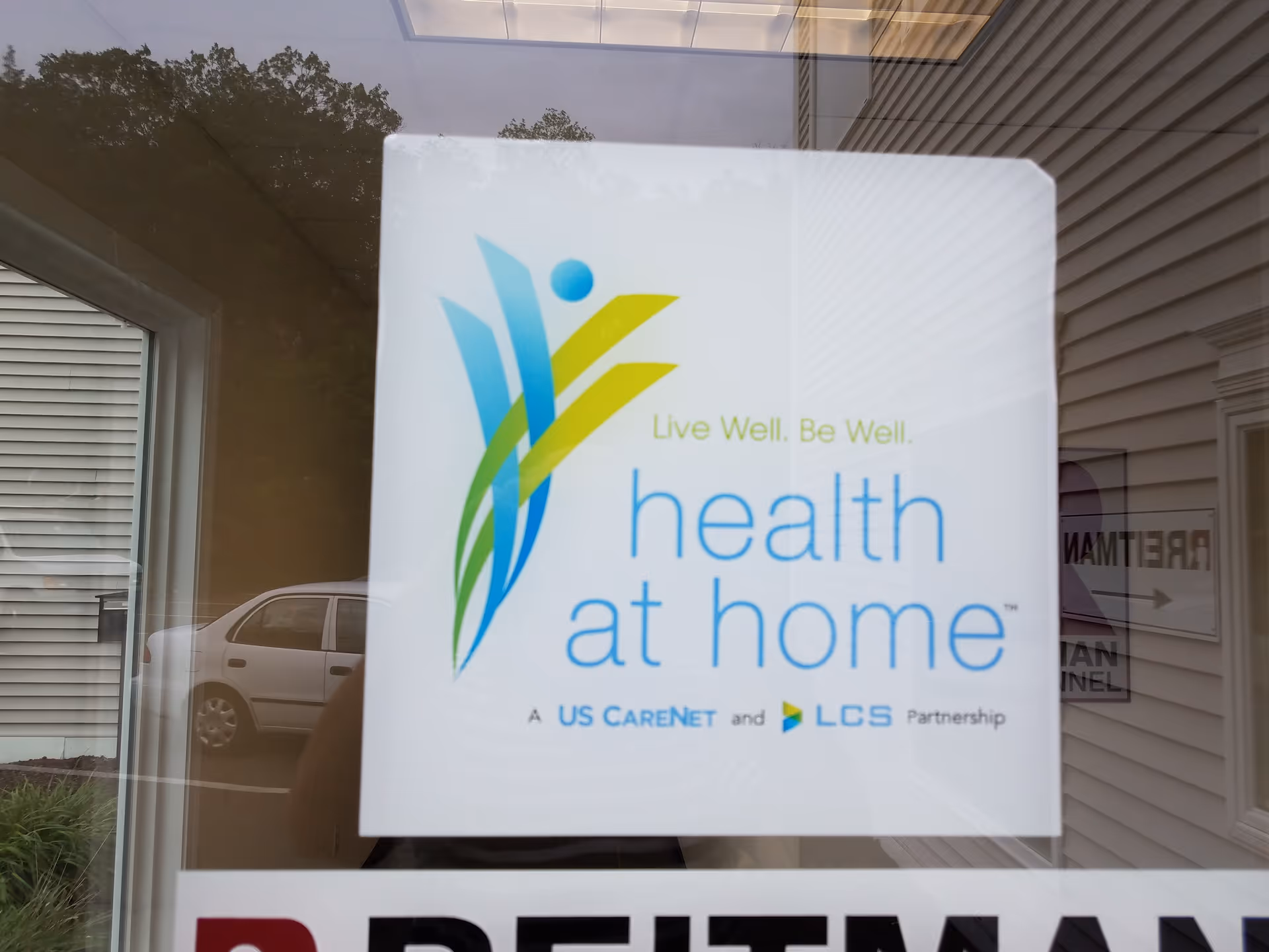 Window sign reading 'health at home' with colorful logo reflected in glass.