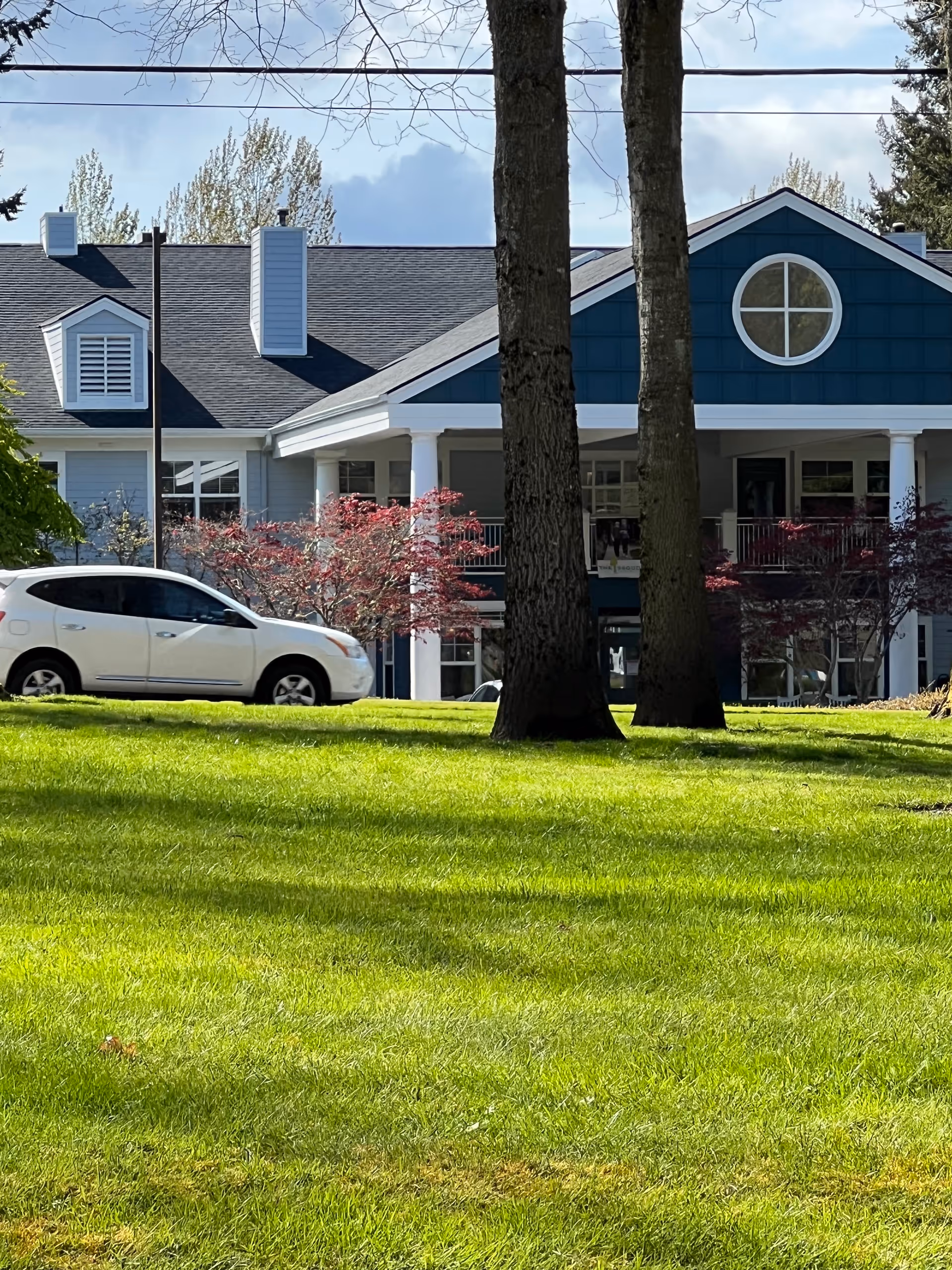 Exterior view of The Sequoia Assisted Living Community with blue siding, circular window, and green lawn.