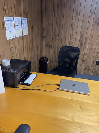 Wood-paneled office desk area with laptop, printer, and a black chair.
